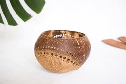 A round, natural-colored candle holder with a textured, perforated design. The candle holder appears to be made of a natural material like wood or ceramic, and has a minimalist, organic style that would complement a variety of home decor styles.