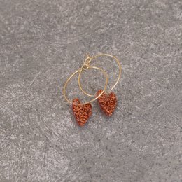  Festive hoop earrings with heart-shaped charms in a copper color. The charms are made of a glittery, sparkling material that adds a touch of holiday charm.