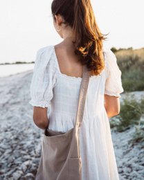 Mocha-colored canvas shoulder bag with puff sleeves and a flowy, ankle-length dress in a natural setting.