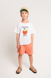  Kids jumpsuit with a graphic t-shirt and orange shorts, featuring a peach-colored fruit graphic and text "Apfelschorle Tasting Club".