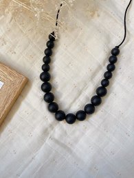 A black beaded necklace with a pendant, suitable for breastfeeding and carrying. The necklace features round black beads and a pendant.