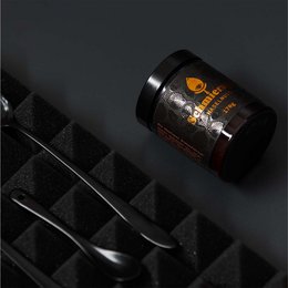 Dark brown hazelnut spread in a glass jar with a black label. The spread has a smooth, creamy texture and is suitable for use as a topping or ingredient in various recipes.