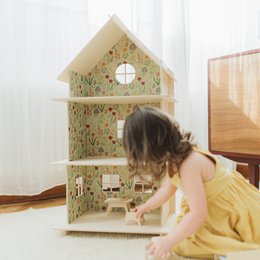 A large, multi-story wooden dollhouse with modern design elements. The dollhouse features multiple rooms and levels, providing ample space for imaginative play.