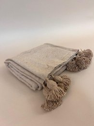 Plaid wall mirror with pompom tassels, camel beige neutral colors, woven textile design, decorative fringe trim.