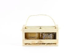 A wooden gift box containing blossom honey and herbal tea. The box has a natural, rustic appearance with a light-colored wood frame and a label indicating the contents.