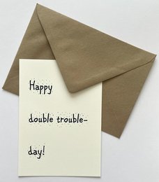 A6 card with handwritten text "Happy double trouble day!" on a white card with a brown envelope.