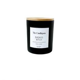 A tall, round black candle with a bamboo lid. The label reads "The Candle Room" and "Badass B * tch" in white text on a black background.