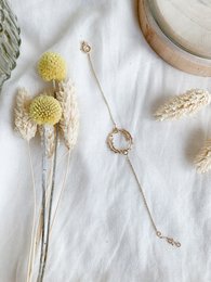 Delicate gold-toned bracelet with circular charm, complemented by dried yellow flowers and natural fibers.