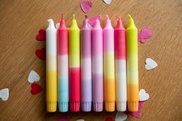 Colorful, multi-dipped candles in various pastel shades including pink, yellow, and purple. The candles have a unique, layered design with a tapered shape.