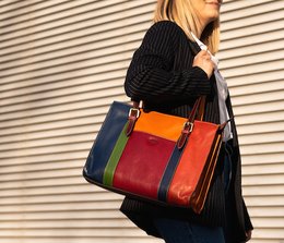 Colorful leather tote bag with bold stripes in red, orange, and navy. Features a structured silhouette, dual top handles, and a zippered main compartment.