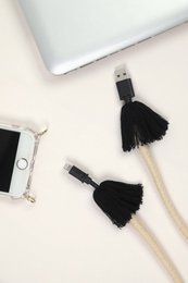 Kaia USB shoulder strap in natural and black colors, featuring tassel accents and a USB cable for charging smartphones.