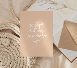 A pink greeting card with the text "I'm happy to have a friend like you" in white lettering. The card is being held in a hand against a light background with some greenery.