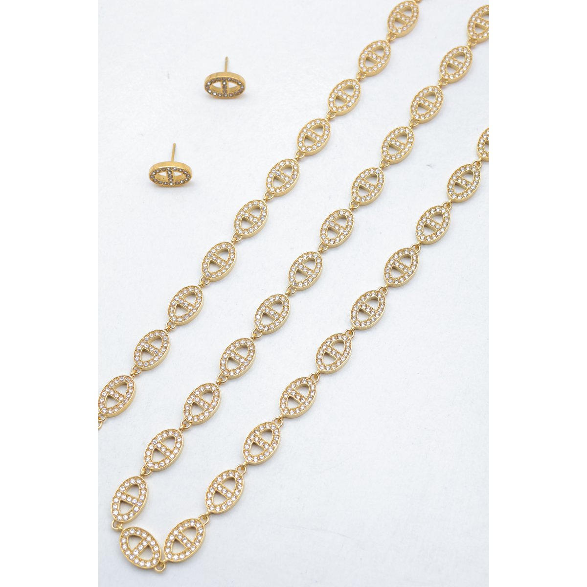 Ensemble assorti comprenant un collier, un bracelet en chaîne et une paire de boucles d'oreilles puces. Chaque bijou est composé d'une succession de maillons en forme de maille marine entièrement pavés de petits strass scintillants.