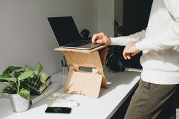 A height-adjustable standing desk converter in natural, navy blue, caramel, red, black, and white colors. The converter allows users to easily transition between sitting and standing while working.