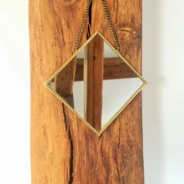  Square brass mirror with diamond-shaped glass panel mounted on rustic wooden board.