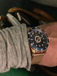 Rose gold watch with black dial, stainless steel case, and mesh band. Features 10 ATM water resistance.
