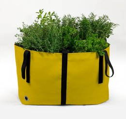 A large, rectangular fabric planter in a vibrant yellow color, featuring lush green plants and foliage. The planter has two handles for easy portability.