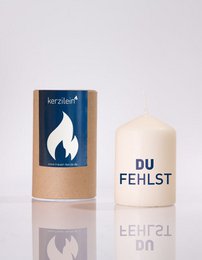 White pillar candle with dark blue kraft packaging, flame design, text "du FEHLST" German message candle.