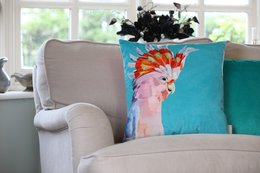 A vibrant, colorful cushion featuring a close-up portrait of a Major Mitchell's cockatoo bird against a turquoise background. The cushion has a soft, velvet-like texture and appears to be a decorative accent piece for a living room or bedroom.