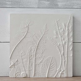 A white, textured wall relief with abstract, nature-inspired patterns and shapes. The relief features a minimalist, organic design with raised lines and textures that create a serene, calming aesthetic.