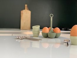 Egg cups in sand and green colors, designed for serving and holding eggs. Includes utensils for preparing and serving eggs.