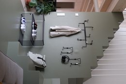 A modern, minimalist clothing rack with a sleek, black metal frame and multiple hanging rods for organizing and displaying clothes. The rack is placed against a light green wall, creating a clean and stylish look.