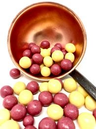 Assorted colorful chocolate-covered puffed rice and mango candies in a wooden bowl.