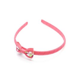 A pink headband with a small bow and a heart-shaped charm in a red and white Liberty Betsy print pattern. Suitable for children.