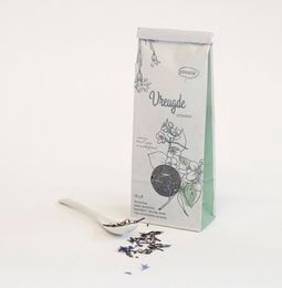 A tall, round glass canister filled with dark tea leaves, labeled "Thee 'Vreugde schenken'" on a white background.