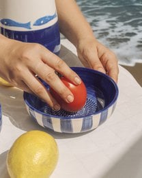 A round, multi-functional grater in a blue and white speckled pattern. The grater is available in small, medium, and large sizes, with and without packaging.