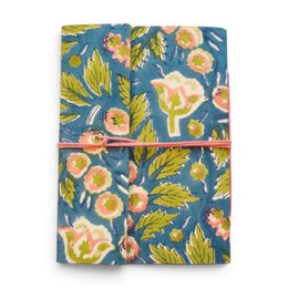 Notebook covered with violet printed fabric featuring floral patterns and designs.
The notebook is covered in a violet-colored printed fabric with a floral pattern. The design includes stylized flowers and leaves in shades of purple, blue, and pink. The fabric has a textured, embroidered-like appearance, adding visual interest to the notebook cover.