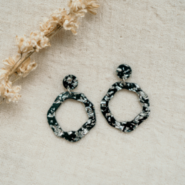 Statement earrings with a black and white floral pattern, featuring a circular hoop design. The earrings have a modern, stylish appearance that would complement a variety of outfits.