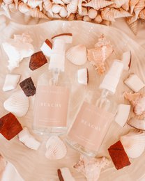 Beachy room spray, clear glass bottle, peachy nude color, coastal fragrance, decorative styling with crystals and shells.