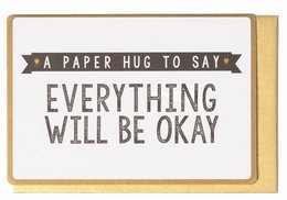 A paper card with the text "A paper hug to say everything will be okay" printed on it. The card has a rustic, handwritten style font and is framed by a simple gold border.