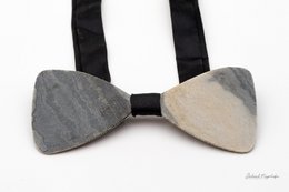 A stylish bow tie made of natural stone, featuring a rustic and unique design. The bow tie has a sleek black strap and a distinctive stone pattern that adds a touch of elegance to any outfit.