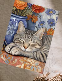  A sleeping tabby cat nestled among vibrant orange and blue flowers on a postcard.
