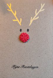 A Christmas card featuring a minimalist design with white antlers and a red pom-pom nose, creating a reindeer-like image. The card is printed on a gray background with the text "Fyne Freeshiyan" at the bottom.