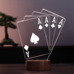 A wooden table lamp with a design of four aces playing cards on a dark background with a silhouette of a tree in the distance.