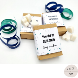  Handmade soap in a gift box with a playful "You did it!" message. The soap is white and the box is decorated with colorful ribbons in shades of blue and green.