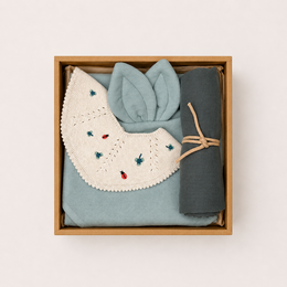 A gift box containing various soft, textured items in shades of yellow and brown, including a teething ring, a rattle, and other baby toys. The box is decorated with a bumblebee motif.