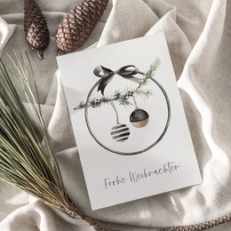A6 greeting card with a minimalist design featuring a wreath of pine cones, berries, and a ribbon bow. The card is printed on textured paper and available with or without a kraft paper envelope.