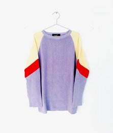 A cozy, oversized kids' sweater in a soft lavender color with contrasting yellow and red panels on the sleeves, creating a retro-inspired look.
