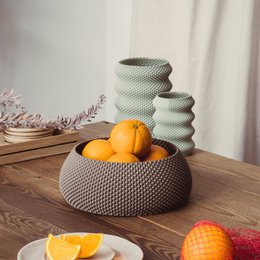 A round, textured decorative bowl in a neutral color palette, suitable for displaying fruit or other decorative items.