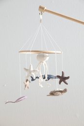 Hanging mobile with white and purple plush sea creatures, including a starfish, turtle, and fish. Wooden frame with hanging elements.