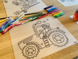 Recolorable placemat featuring a tractor illustration, suitable for kids. Includes details like wheels, gears, and a driver.