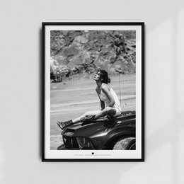 A black and white photograph of a person sitting on the back of a motorcycle in a natural setting with cherry blossoms in the background.