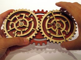 A wooden puzzle game with interlocking gears and cogs in a black box. The game appears to be called "Double Trouble" and is categorized as a game or puzzle.
