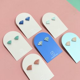 Porcelain stud earrings in a variety of colors and patterns, including dots, nude, minty stripes, kobalt, mint, red, and ocean. The earrings feature a simple, minimalist design with geometric shapes.