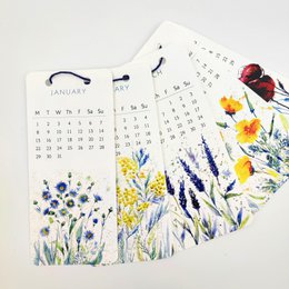 A 2024 wall calendar featuring a variety of colorful meadow flowers, including yellow daffodils, purple lavender, and red poppies. The calendar pages showcase the natural beauty of these floral designs.