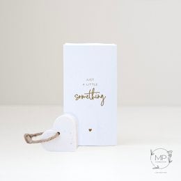 A small, white gift box with the text "Just a little something" printed on it. The box contains a white heart-shaped ornament or decoration.
